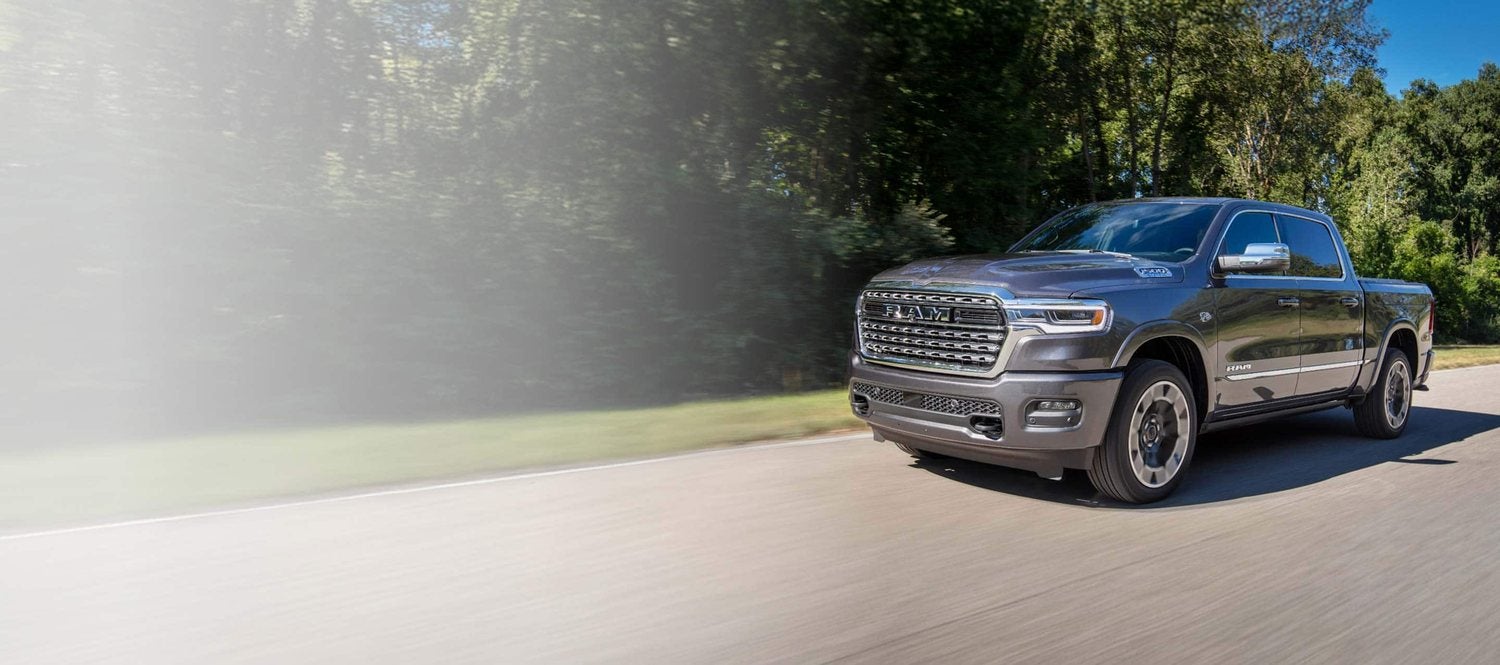 Gray 2026 Ram 1500 Limited 4x4 crew cab driving down a country road in fall