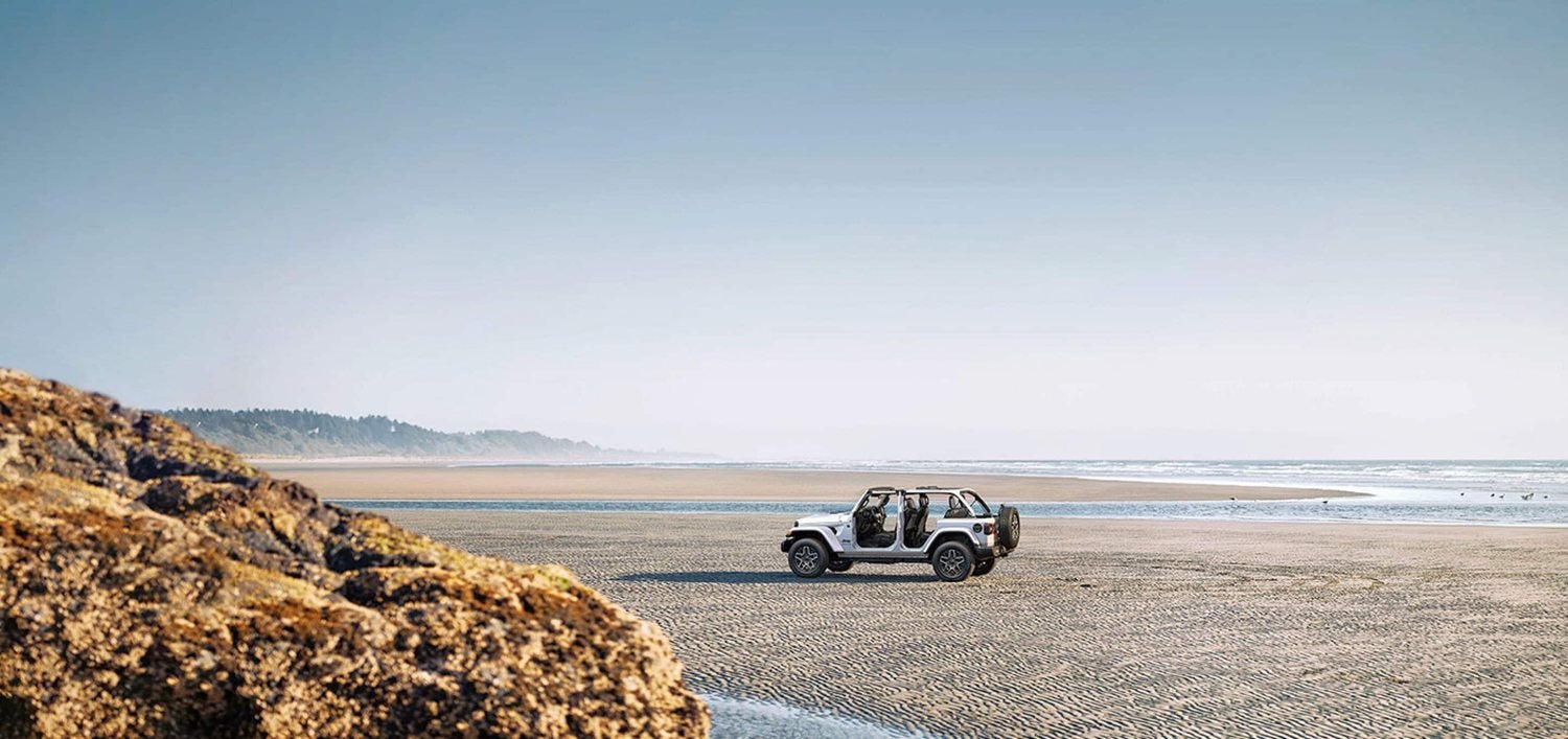 White 2026 Jeep Wrangler Sahara four door with doors and top removed on a beach