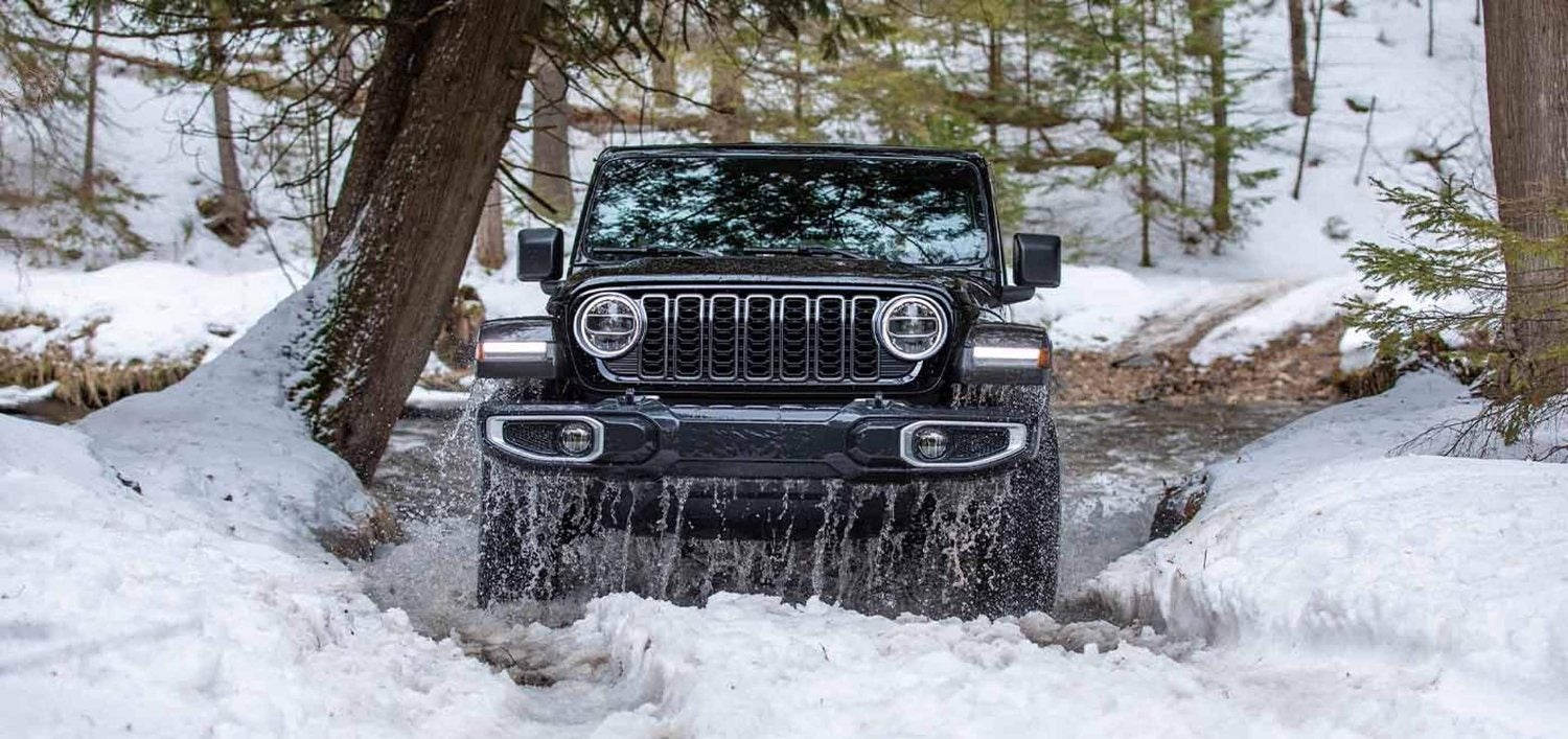 Black 2026 Jeep Wrangler Sahara exiting an icy stream on a snow covered trail
